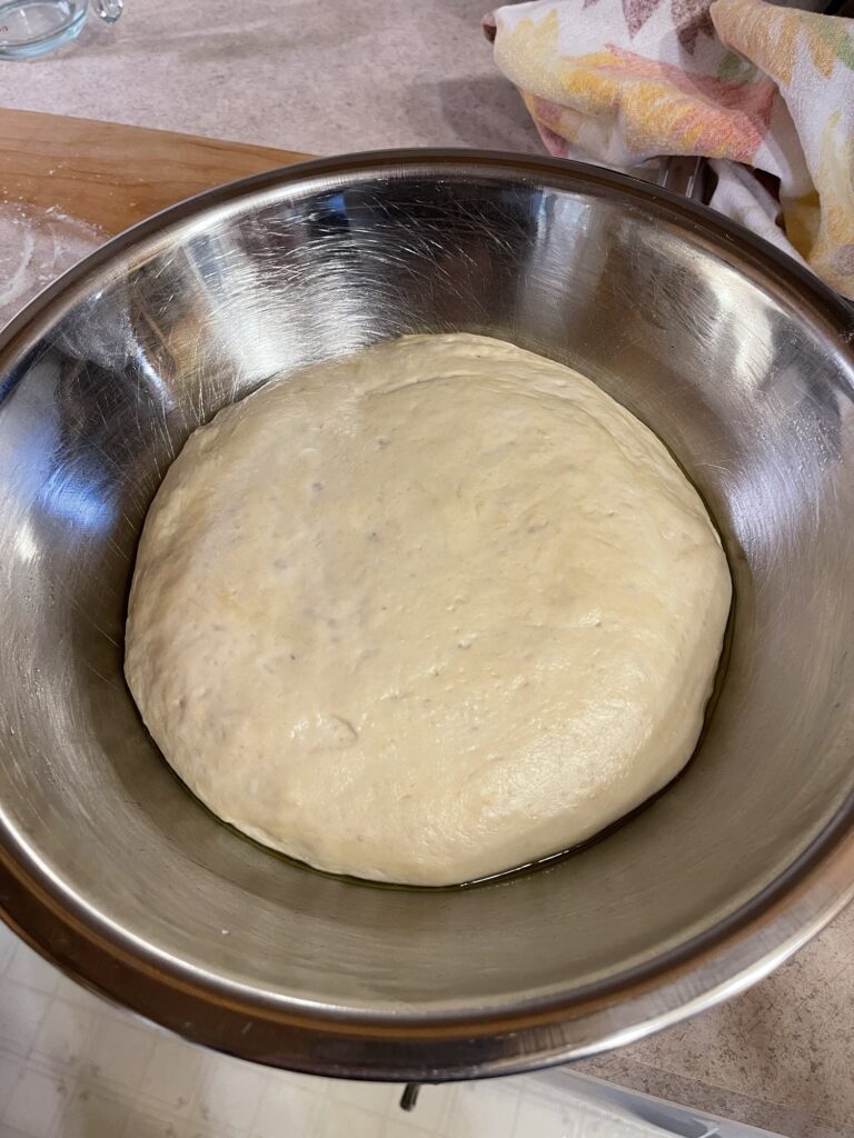 A silver mixing bowl with a somewhat flat mass of beige-colored dough filling most of the bottom half of the bowl.