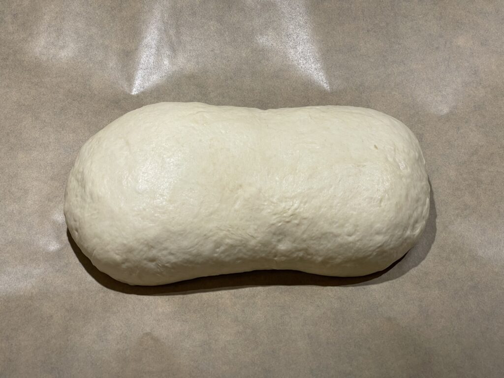 An oblong blob of beige-colored bread dough resting on brown parchment paper
