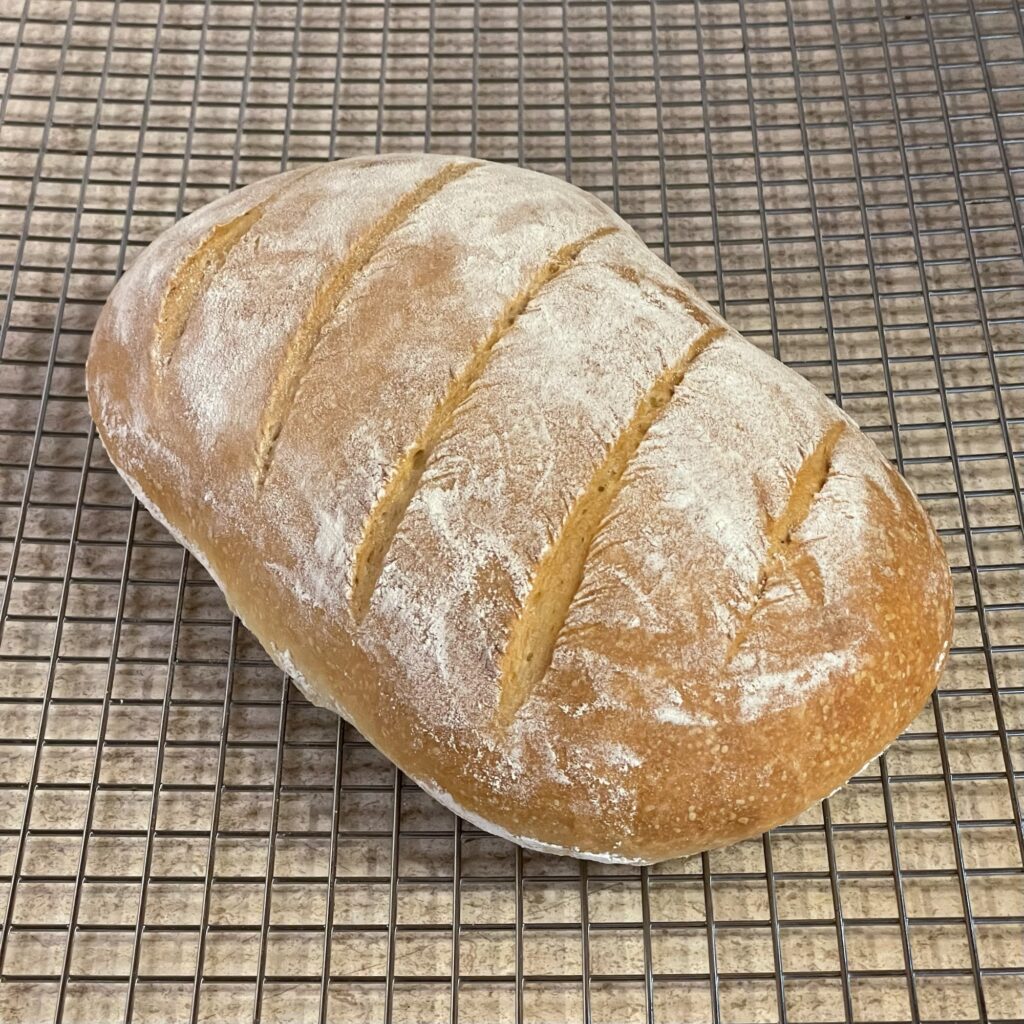 A brown loaf of bread dusted in white flour, resting on a wire cooling rack.
